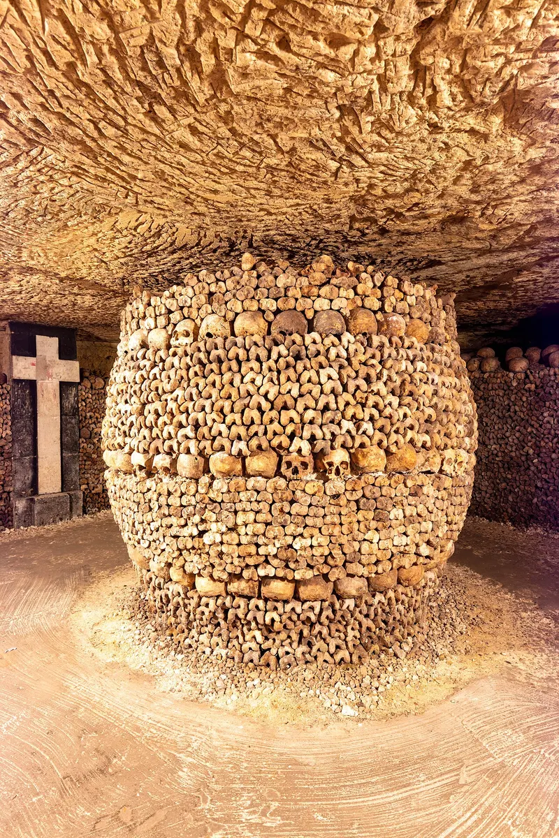 Walls of stacked skulls and long bones lining a gallery of the Paris Catacombs
