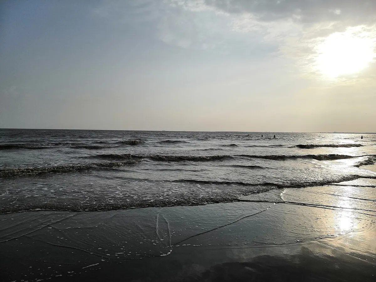 Evening view of the dark sand and shallow water at Dumas Beach near Surat
