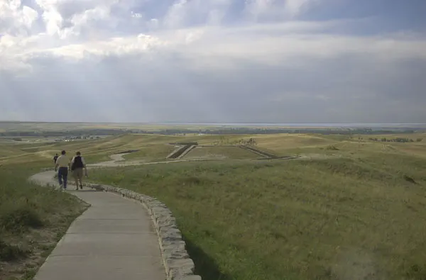 A paved path across the grassy ridges toward the Indian Memorial at Little Bighorn Battlefield under a cloudy sky