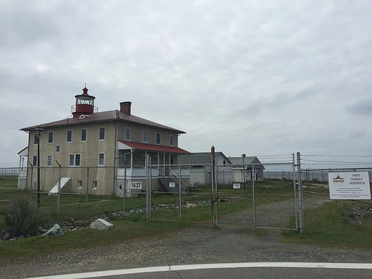 The white two-storey Point Lookout Lighthouse with its rooftop lantern in Point Lookout State Park, Maryland